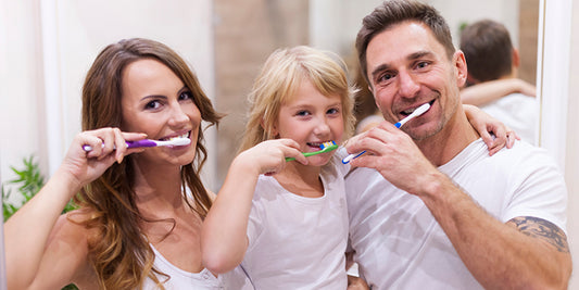 Family of four brushing their teeth together in a bright, modern bathroom.